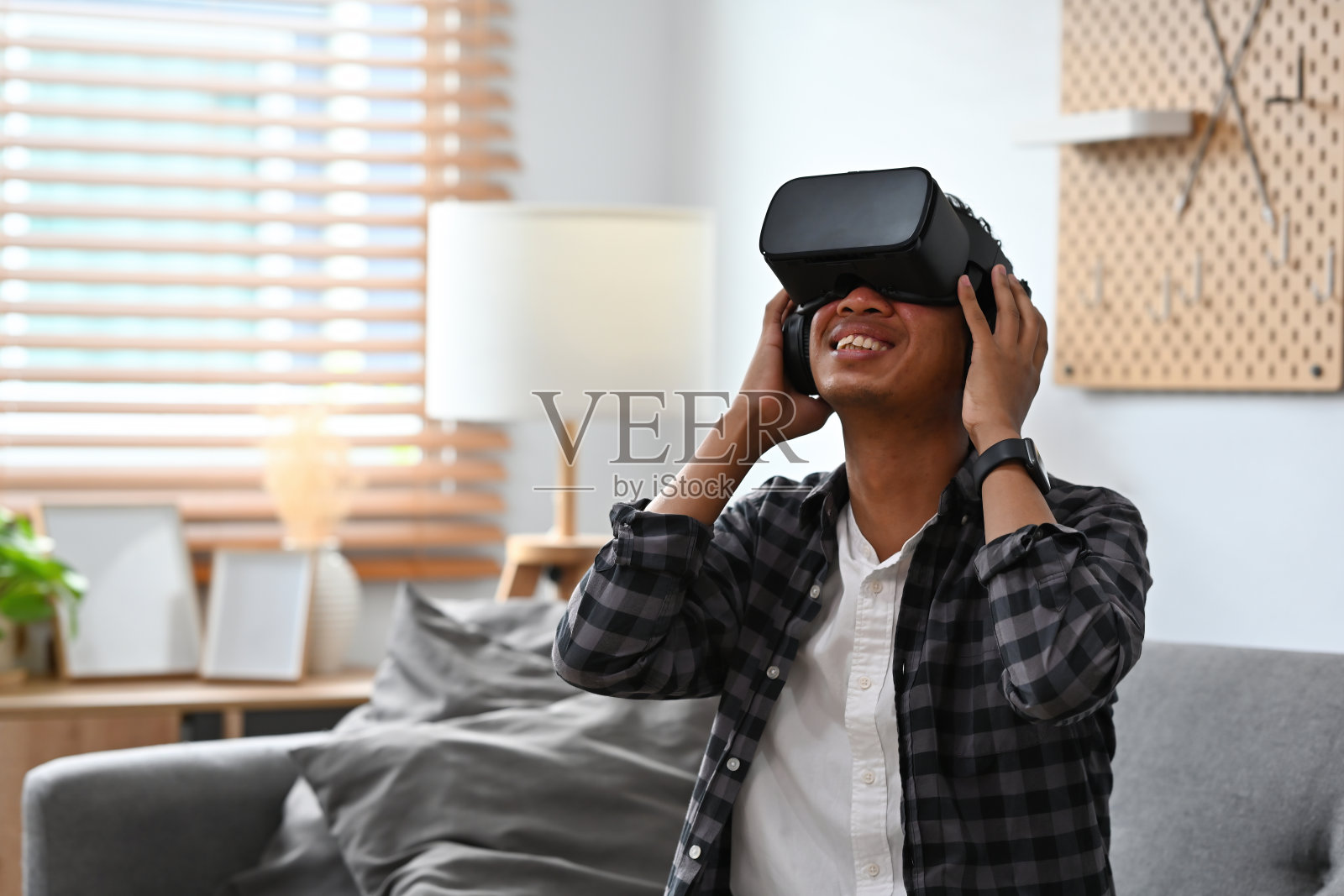 一个男人的肖像坐在客厅的沙发上，戴着虚拟现实技术的眼镜，惊讶地抬头看，为未来，游戏和技术的概念。照片摄影图片