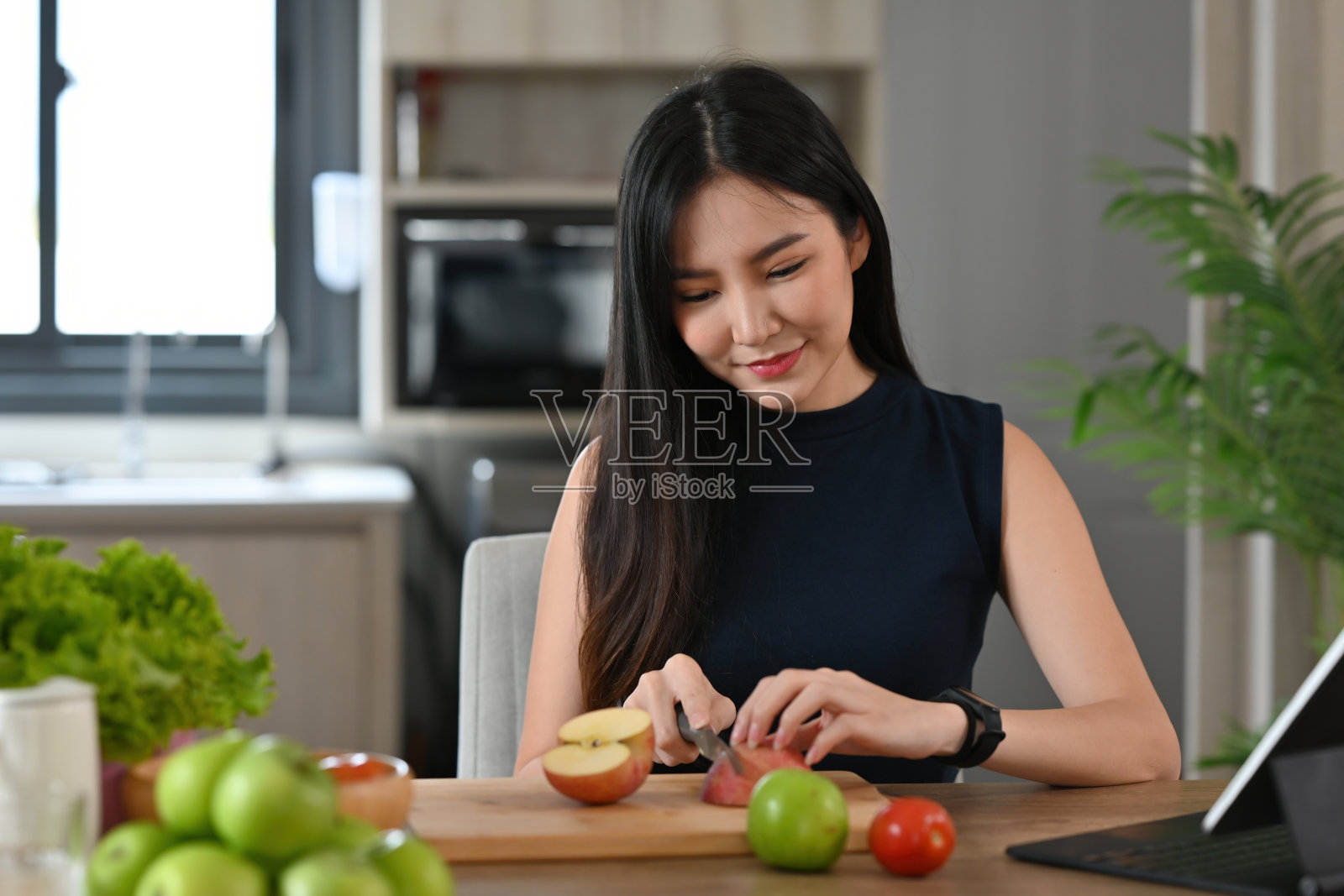 一个年轻漂亮的亚洲女人在木板上切水果和准备一顿饭的肖像，为食物、健康和烹饪的概念。照片摄影图片