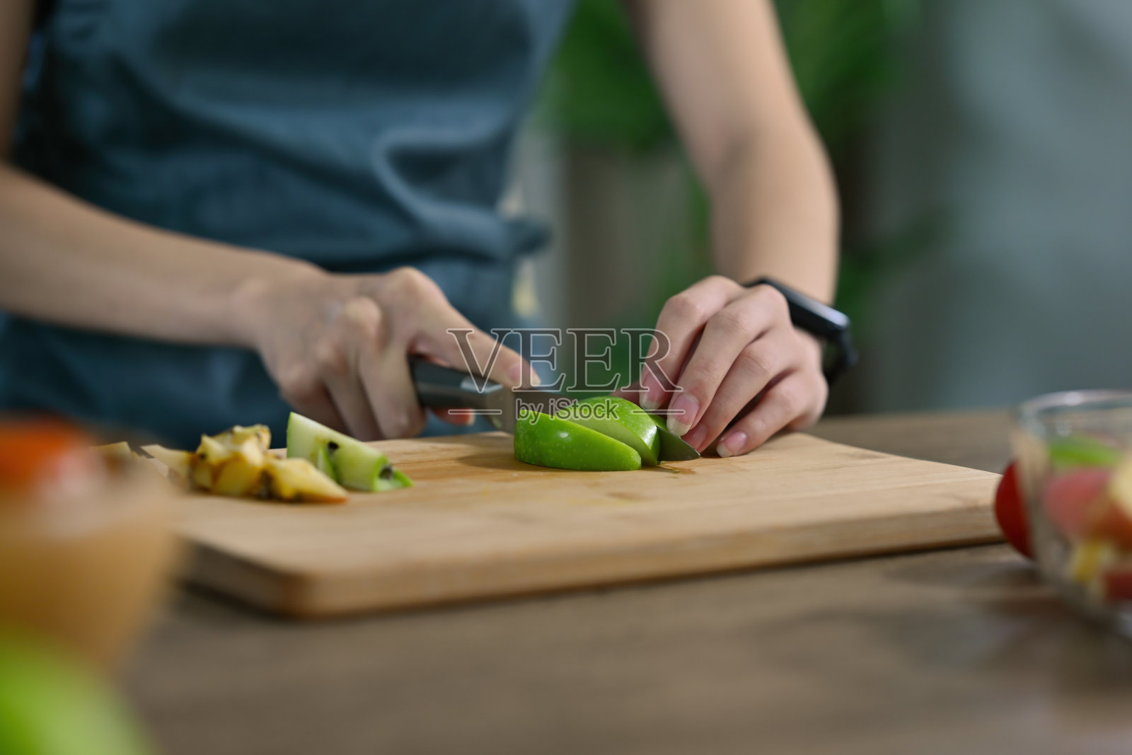 裁剪视图年轻女子的手切青苹果和水果准备一餐在一个木制切板，为食物，健康和烹饪的概念。照片摄影图片