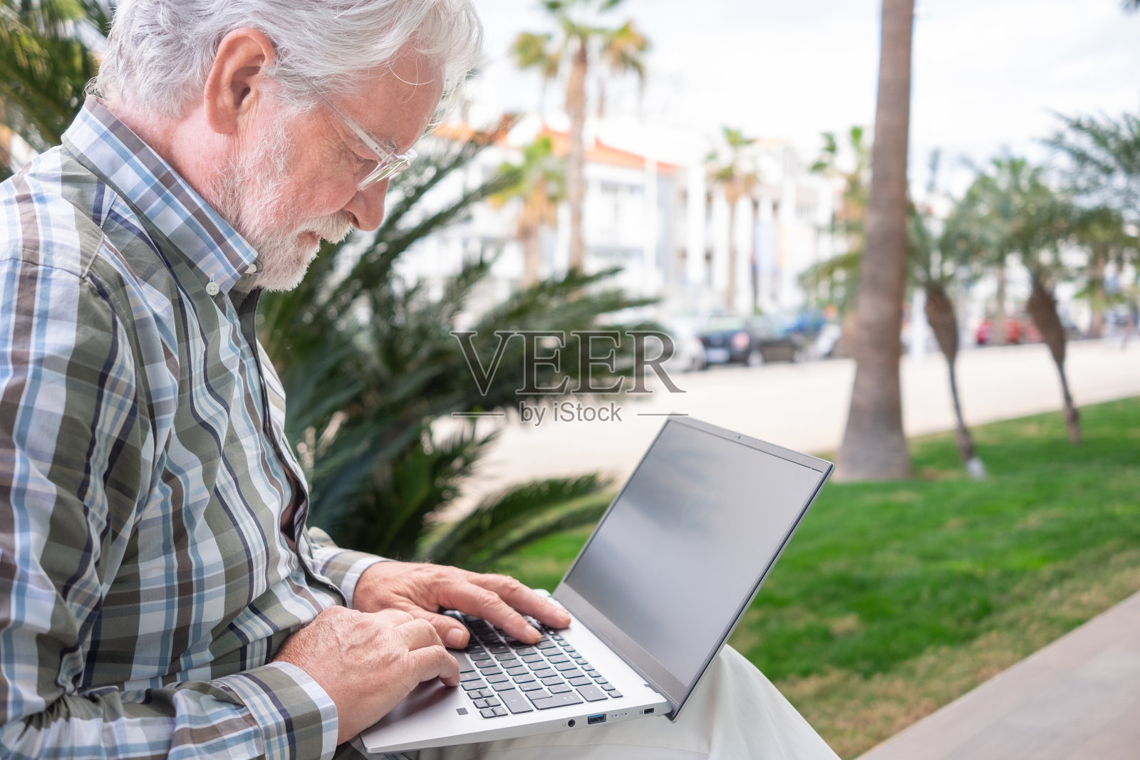 商人坐在公园里用笔记本电脑打字。成熟的大胡子老人在数字笔记本电脑上工作，使用无线技术上网照片摄影图片