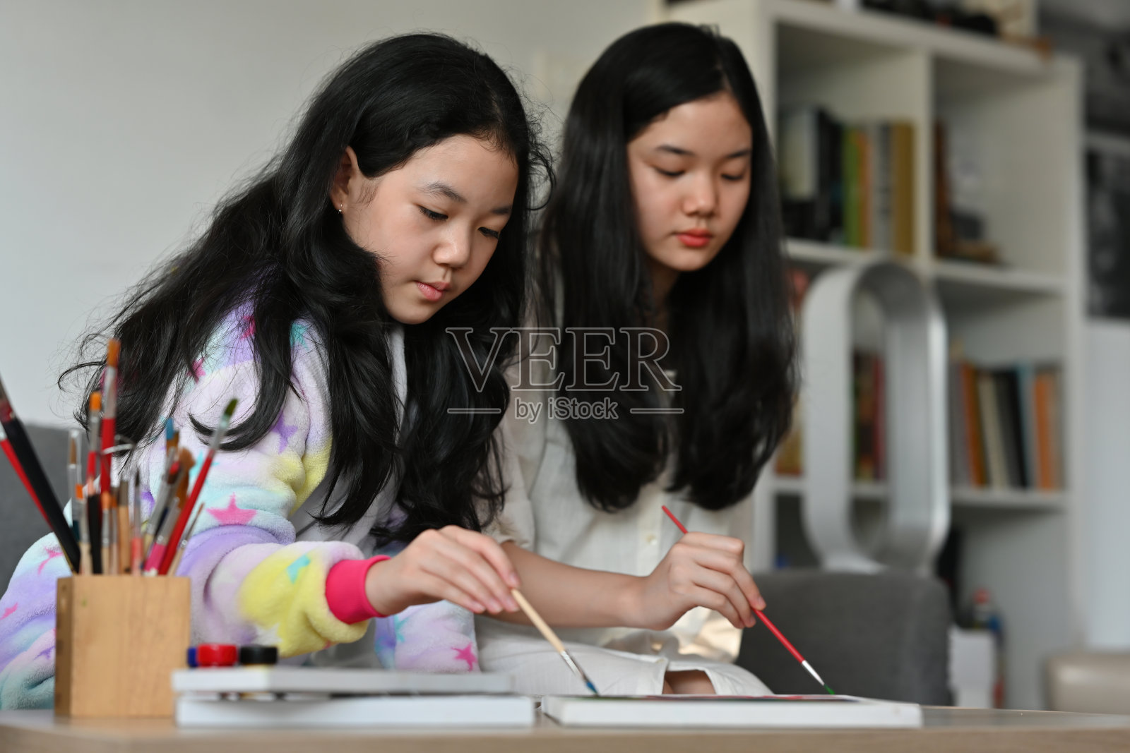 一幅亚洲女孩坐在客厅拿着画笔在画布上工作的肖像，为艺术，教育，家庭和家庭的概念。照片摄影图片