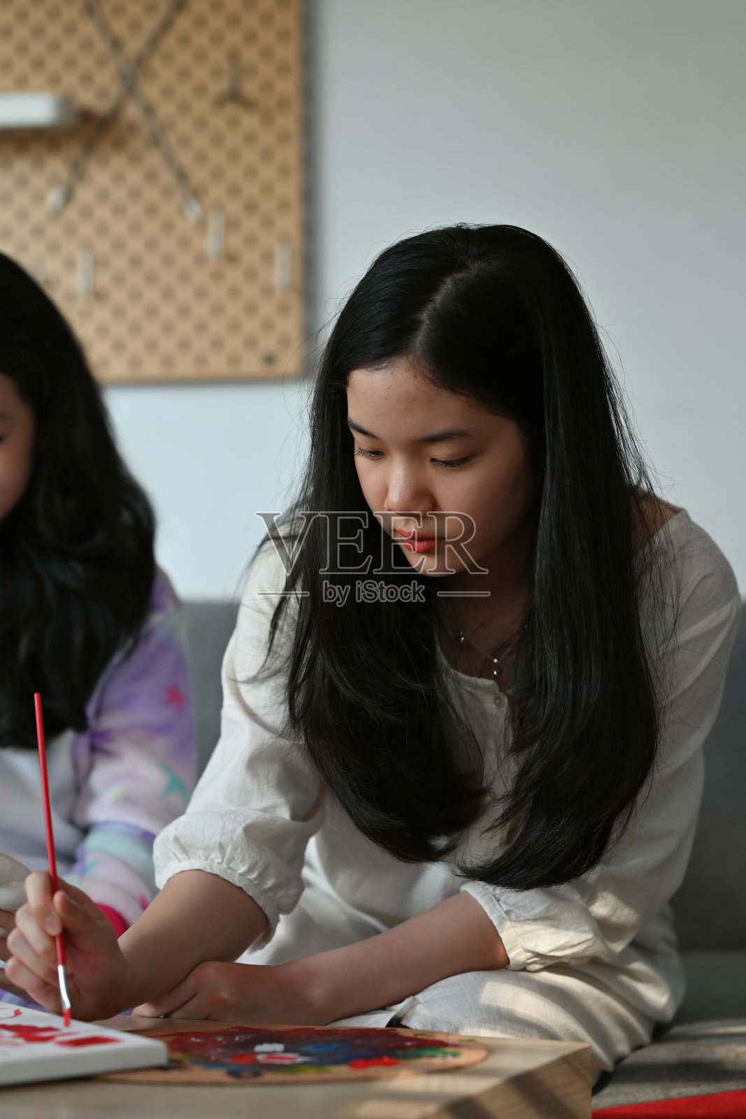 一幅亚洲女孩坐在客厅拿着画笔和朋友在画布上工作的肖像，为艺术，教育，家庭和家庭概念。照片摄影图片