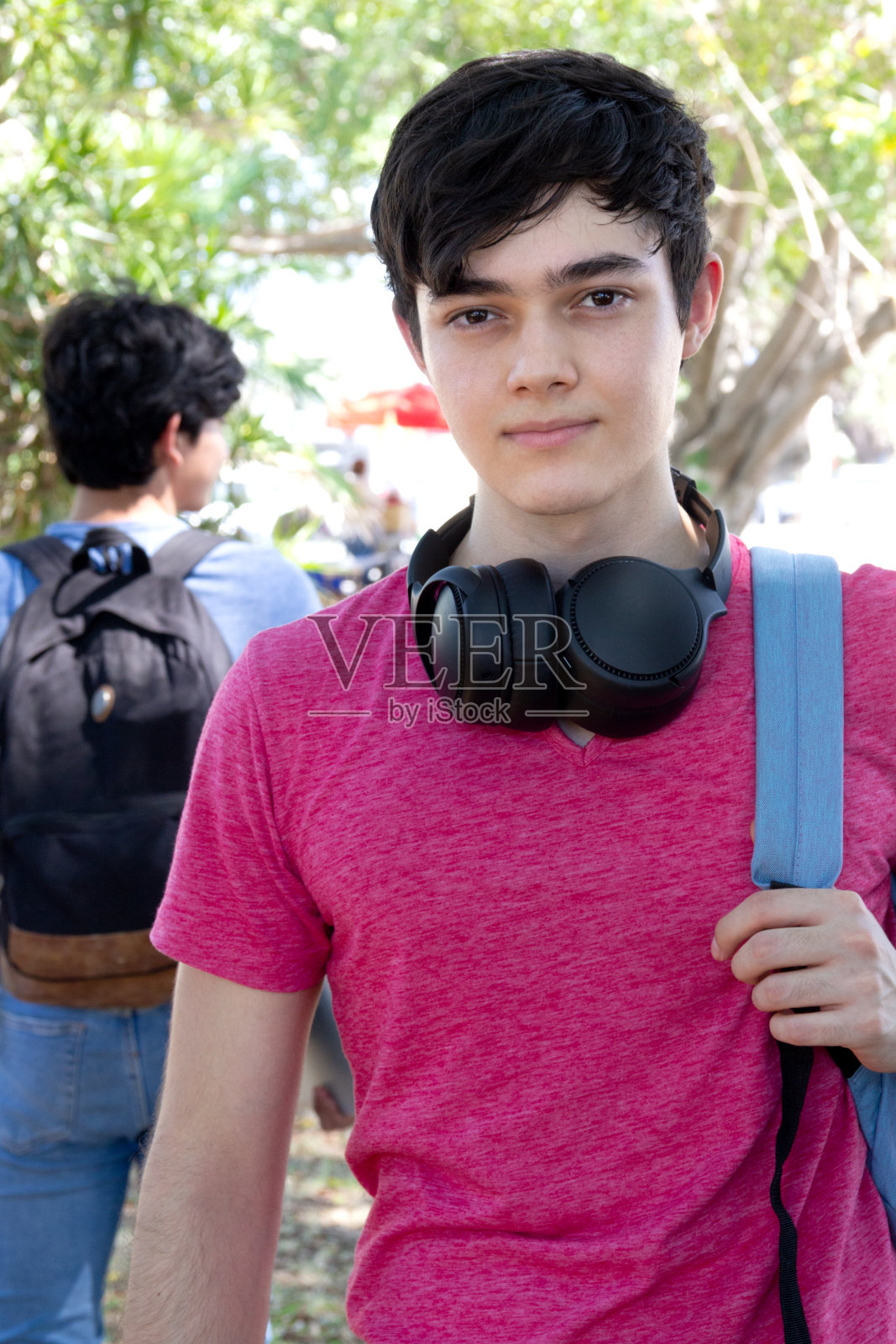 年轻的学生男子背着双肩包，戴着无线耳机照片摄影图片