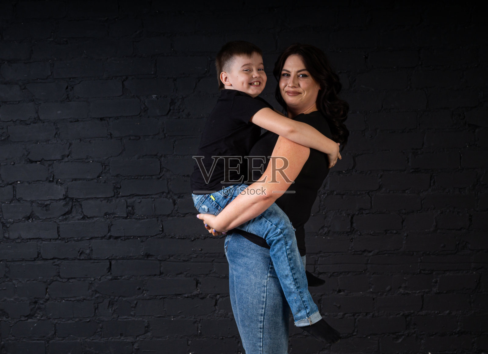 一位身穿黑色连衣裙的母亲抱着她的儿子，坐在一张高椅子上。照片摄影图片