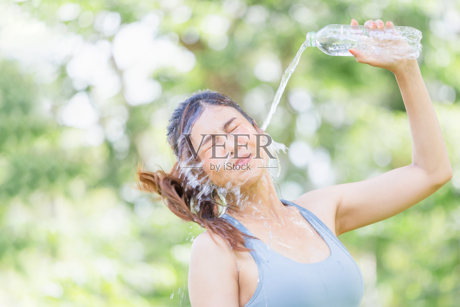 运动员年轻美丽的女子喝和泼水在她的脸在夏天的绿色公园，体育女子从一个塑料瓶喝水后，工作锻炼照片摄影图片