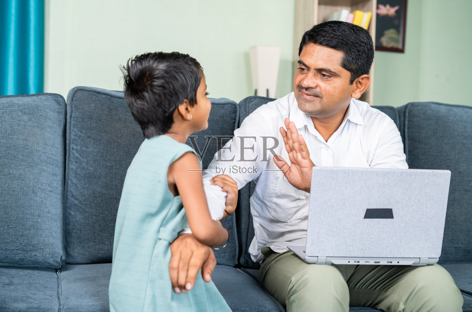 新冠肺炎大流行期间，女儿在家忙着用笔记本电脑工作，打扰了父亲——在家工作、为人父母的概念和新常态。照片摄影图片