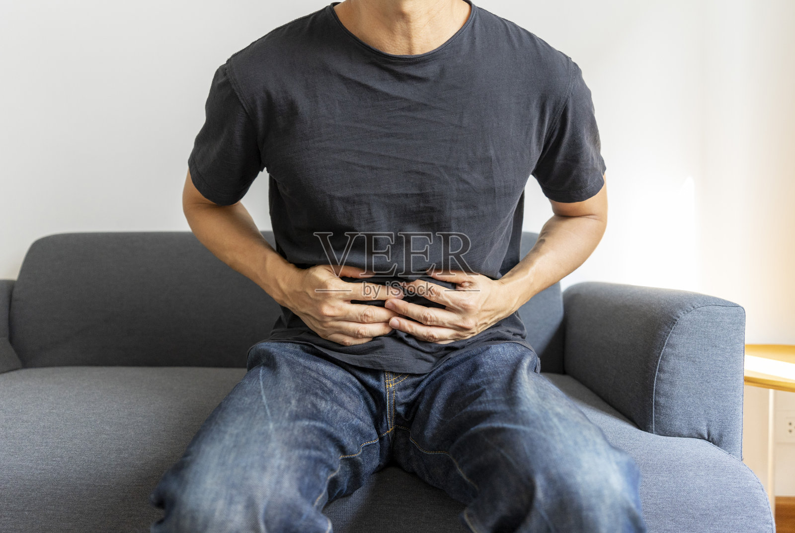 坐在沙发上的男人在家胃痛。照片摄影图片