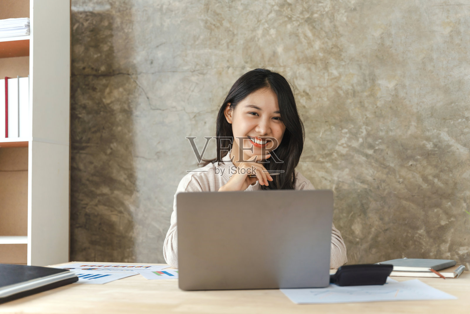 看着相机，快乐的年轻亚洲自由职业的人与笔记本电脑在办公室工作的商业女性。照片摄影图片