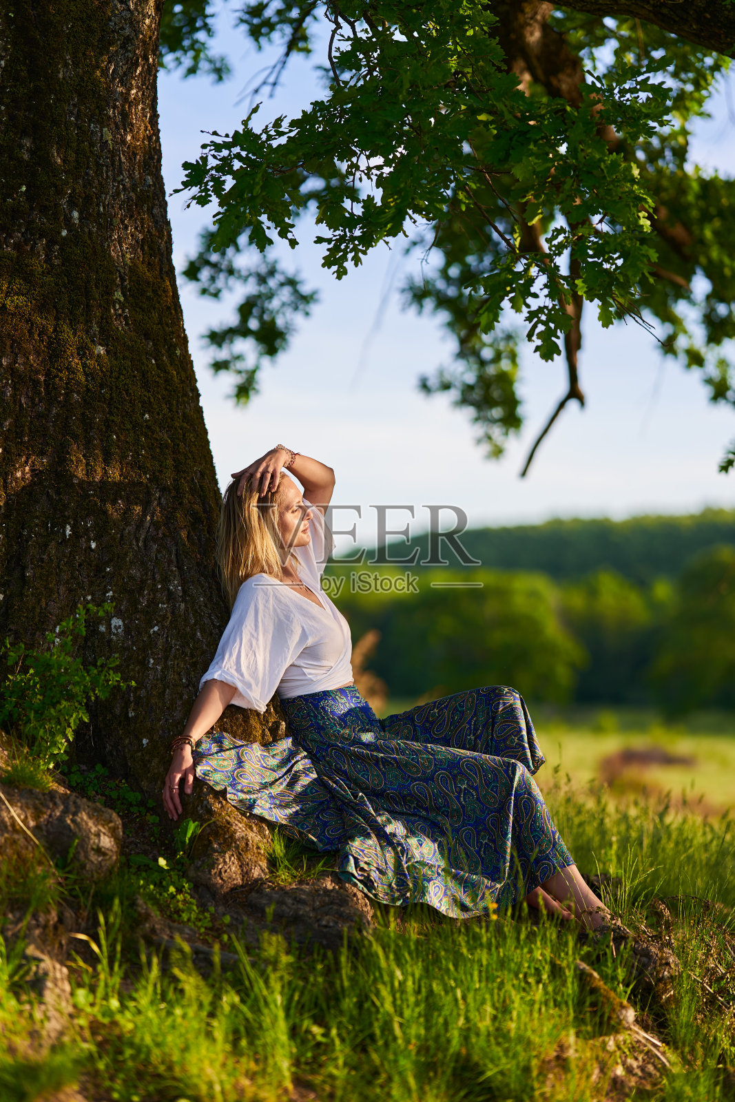 年轻女子在夕阳下的橡树旁摆姿势照片摄影图片