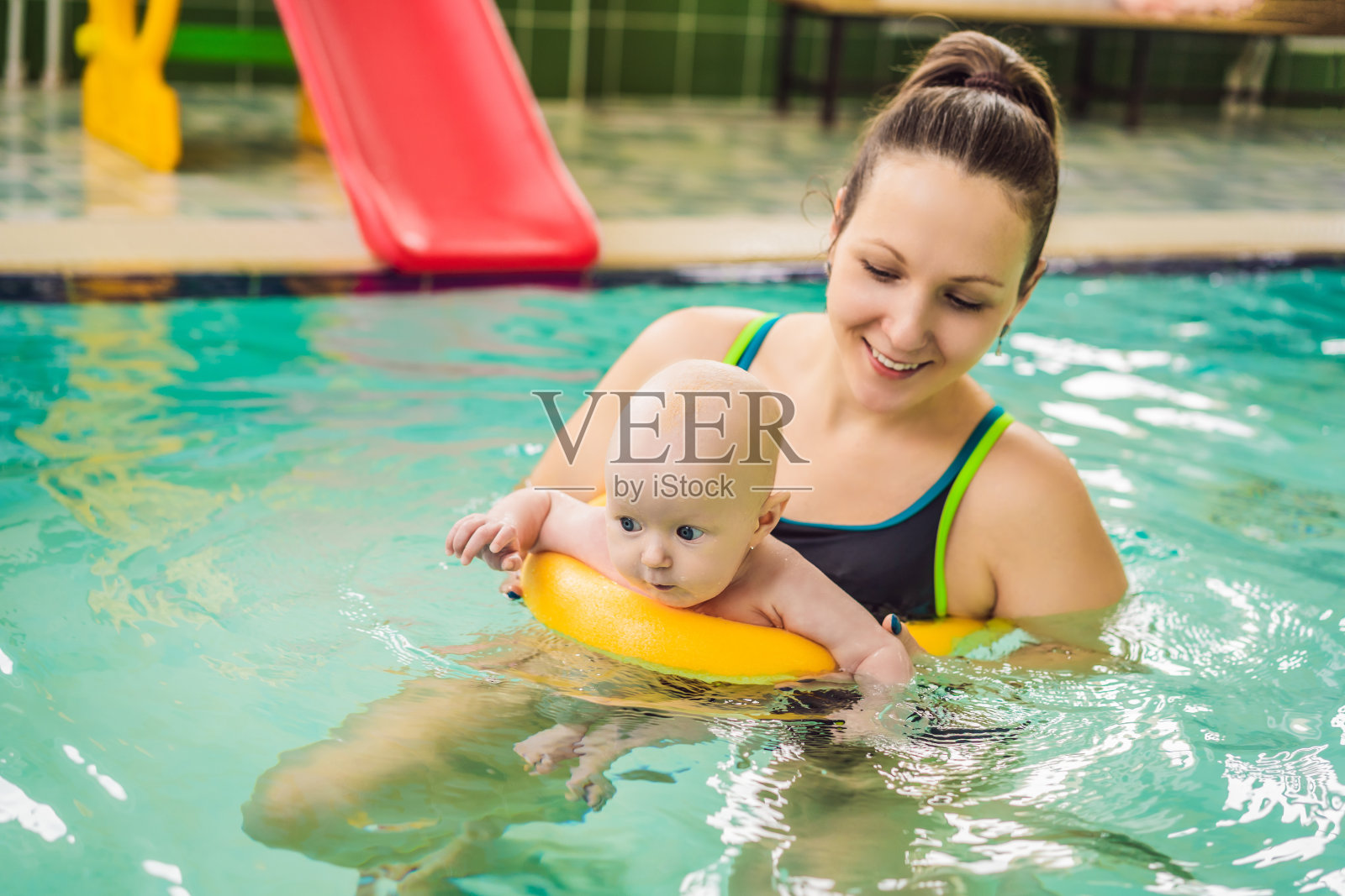 美丽的妈妈在教可爱的女婴如何在游泳池游泳。孩子和妈妈在水里玩照片摄影图片