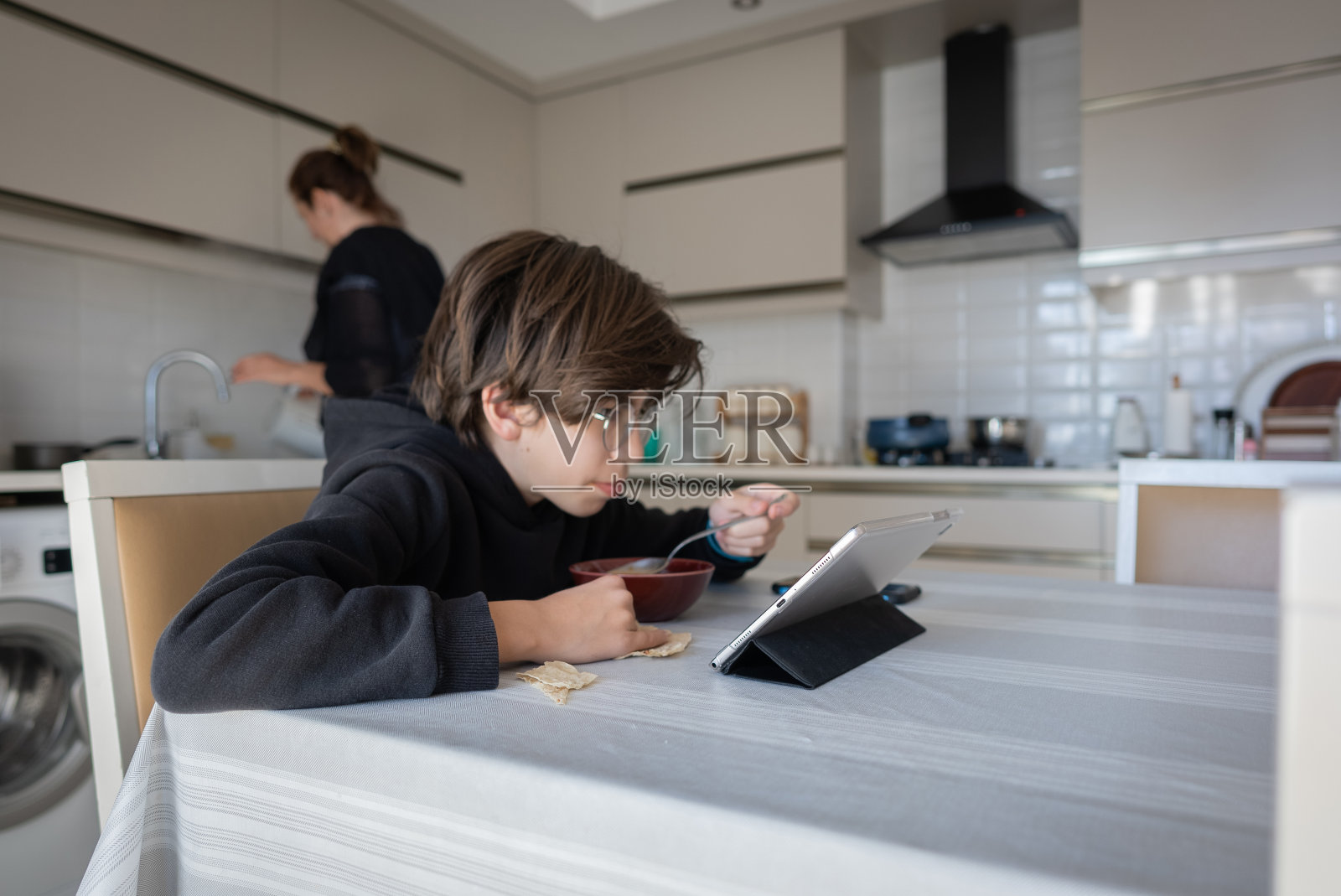 小男孩在厨房边吃边看电影，照片摄影图片