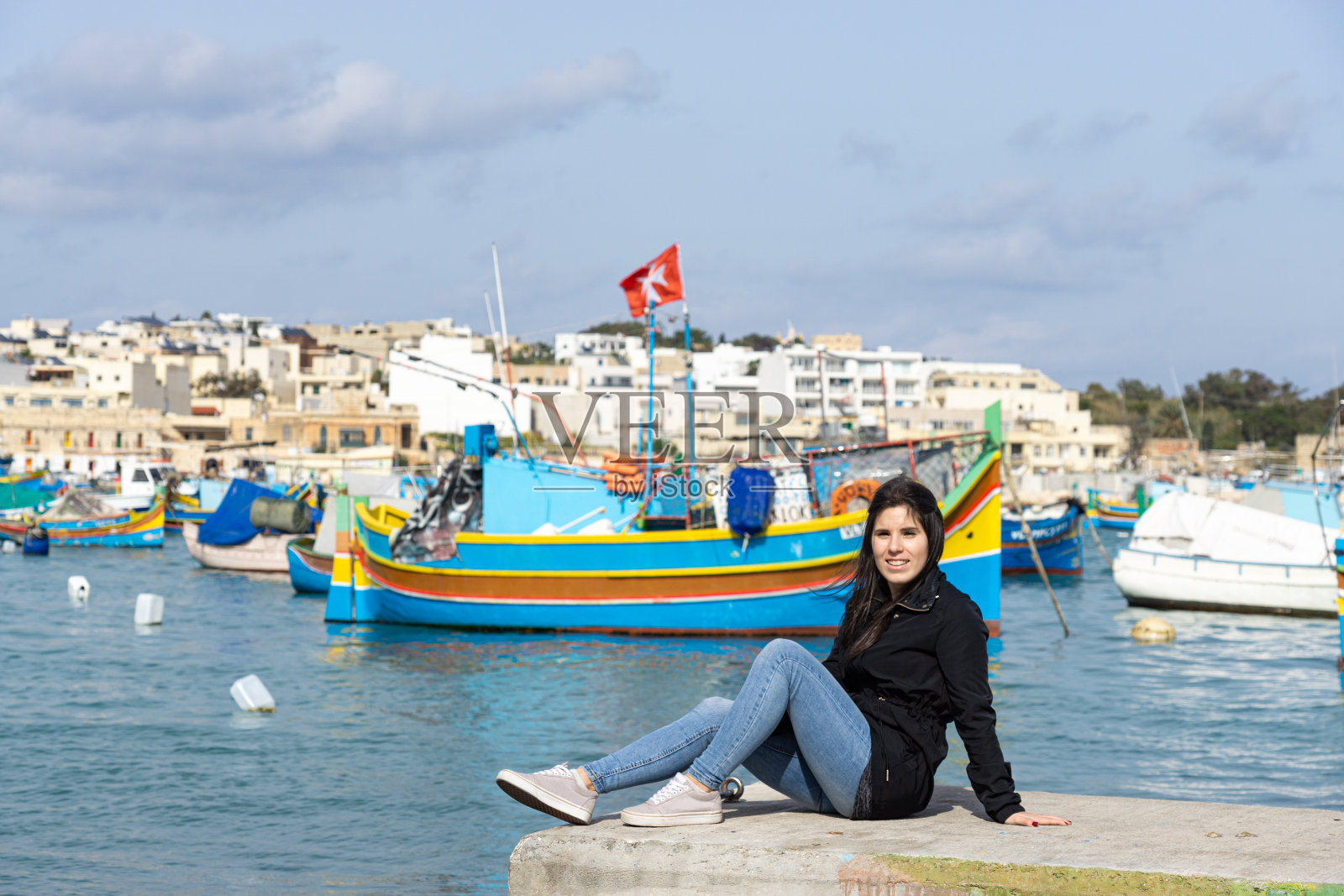年轻的女游客坐在马萨克斯洛克，背景是大海里五颜六色的船照片摄影图片