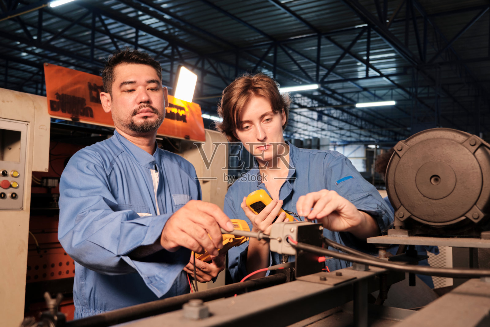 两名专业工程师在工厂检查机器的电气系统。照片摄影图片