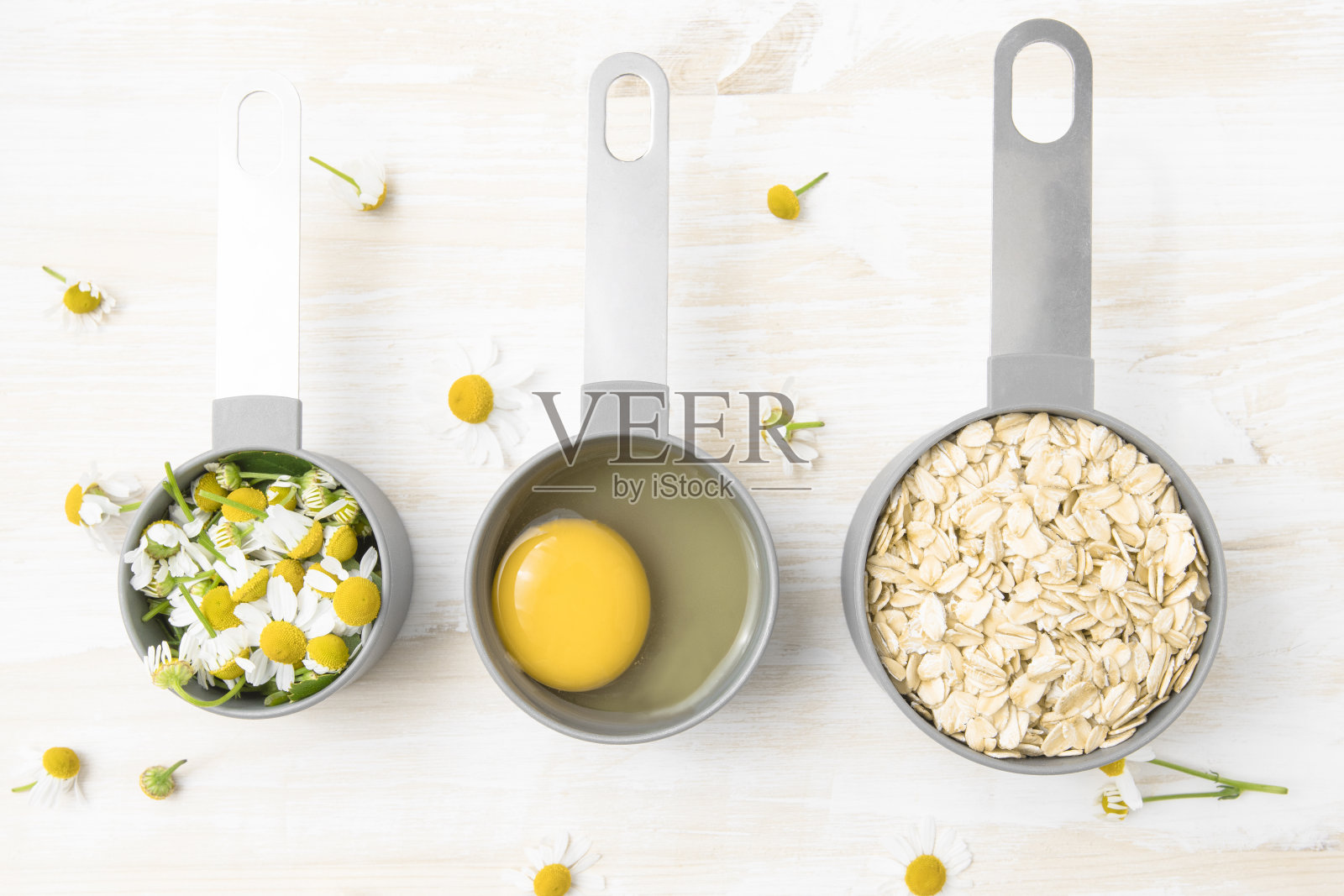燕麦片，洋甘菊花，鸡蛋在白色木板上的杯子俯瞰。做一个适合身体和头发的自制面膜。照片摄影图片