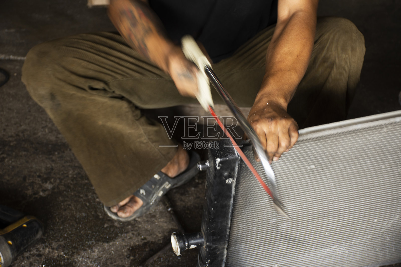 在泰国Nonthaburi的Bang Bua Thong当地的车库车间，专业人员使用手工钢锯工具切割汽车散热器的钢盖和修理车辆照片摄影图片