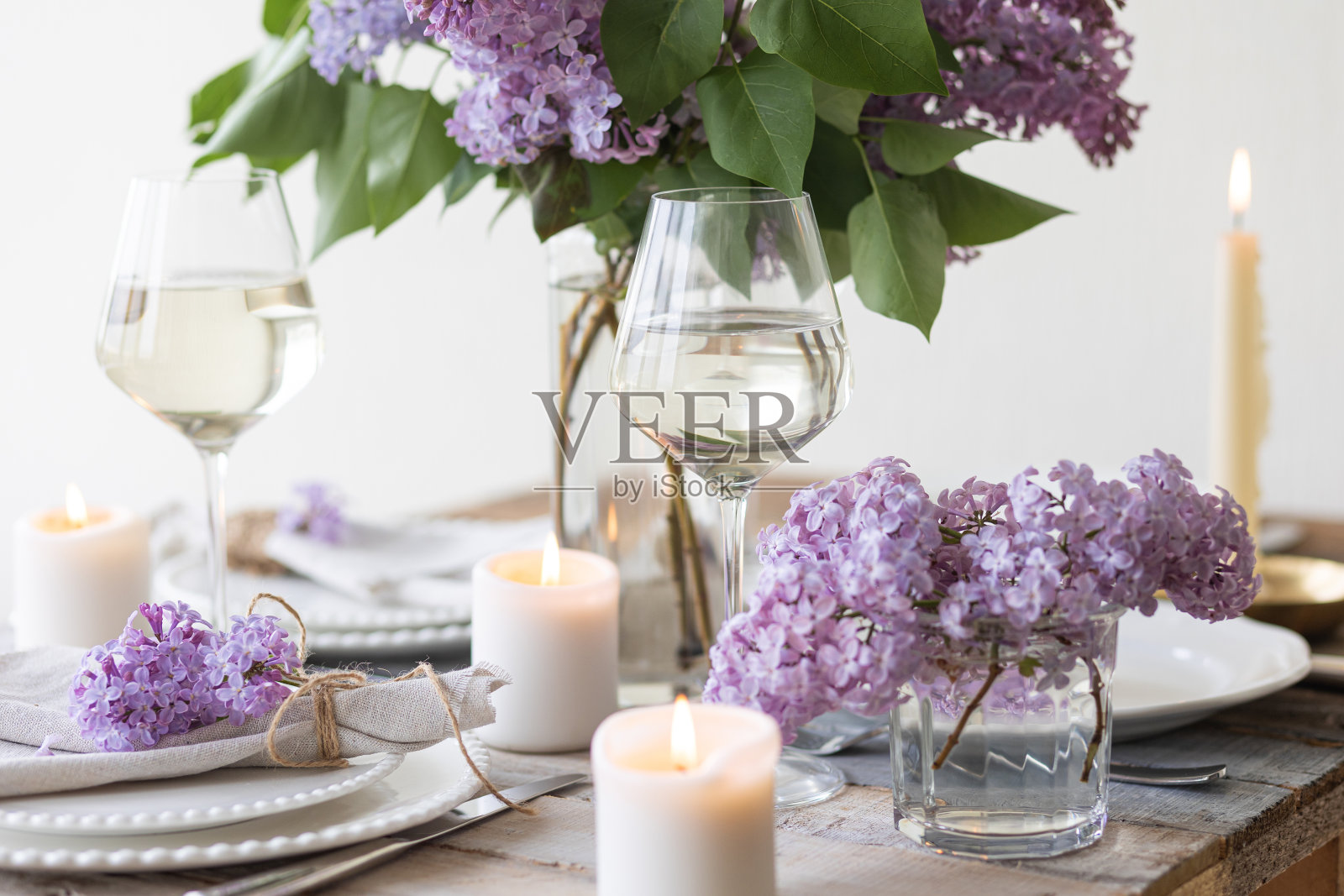 美丽的餐桌装饰与一个春天盛开的丁香花婚礼晚餐。庆祝特殊事件漂亮的白色盘子，葡萄酒杯。乡村风格照片摄影图片