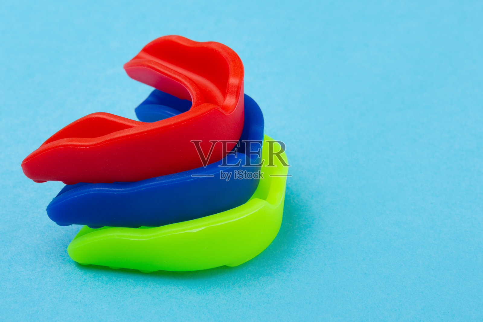 三个蓝色、红色和绿色的拳击护嘴，一个挨着一个照片摄影图片