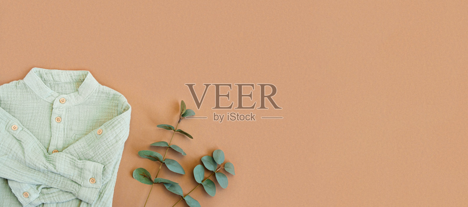 绿色婴儿衬衫与桉树在米色背景与空白的文本。婴儿天然材质配件概念。俯视图，平铺。小男孩波西米亚服饰设计。新生儿天然材料。照片摄影图片