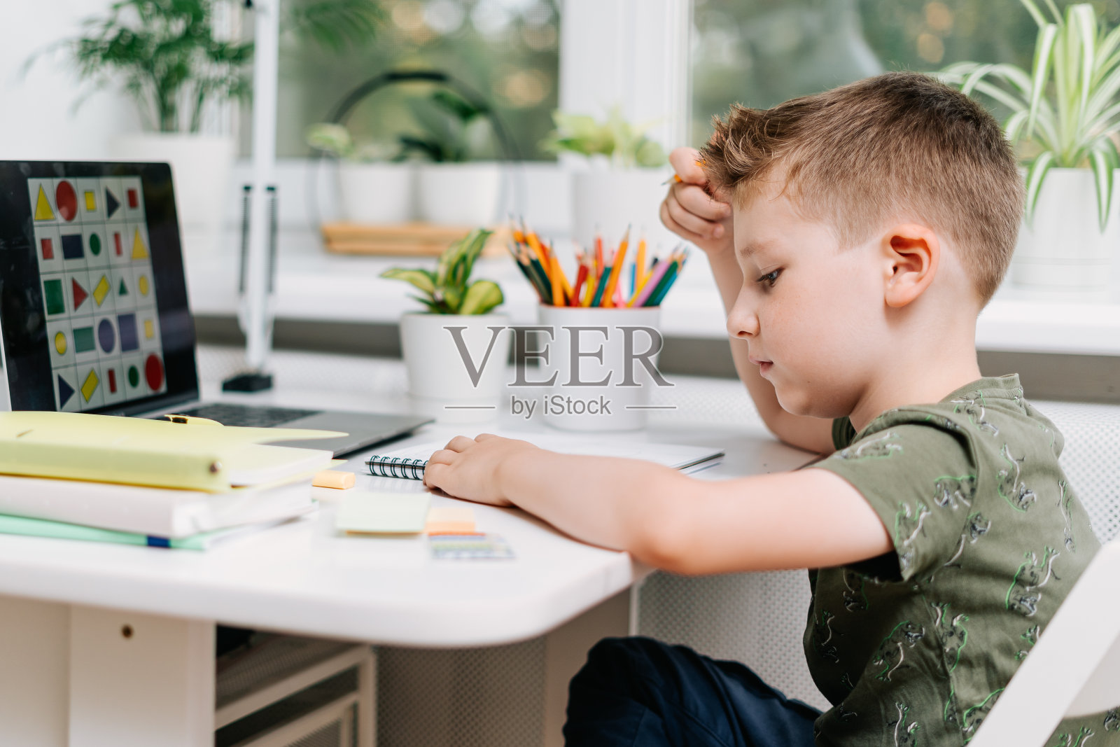 远程学习在线教育。白人微笑小孩男孩在家里用笔记本电脑学习和做作业。思考孩子坐在笔记本，铅笔和训练书。回到学校照片摄影图片