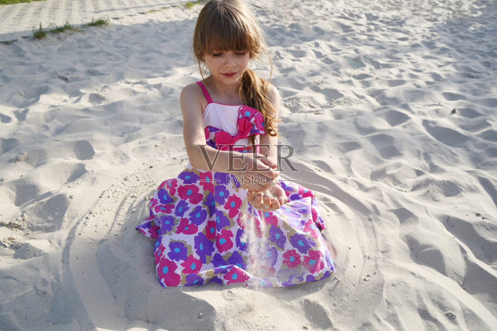 一个7 ~ 8岁的黑发女孩穿着带着大朵花的吊带裙坐在白色的沙滩上照片摄影图片