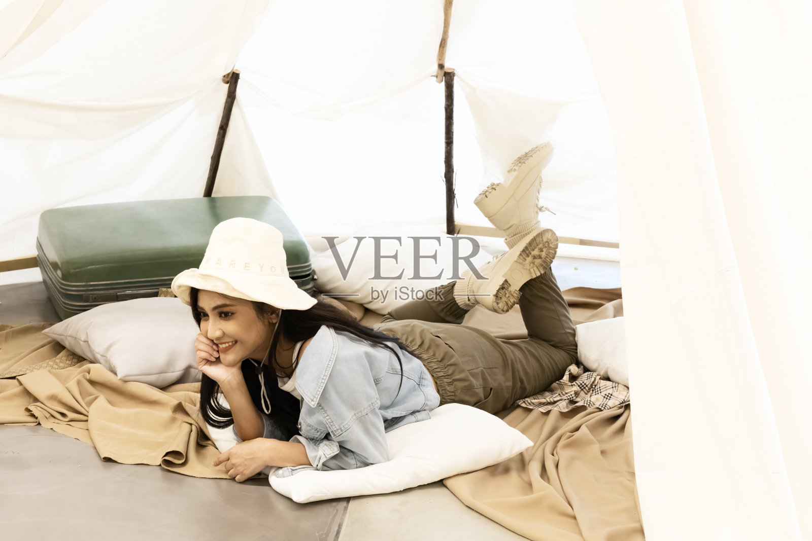 黑色长发的妇女躺在帐篷前微笑着旅行露营。一个女人在旅行野营的一面。照片摄影图片