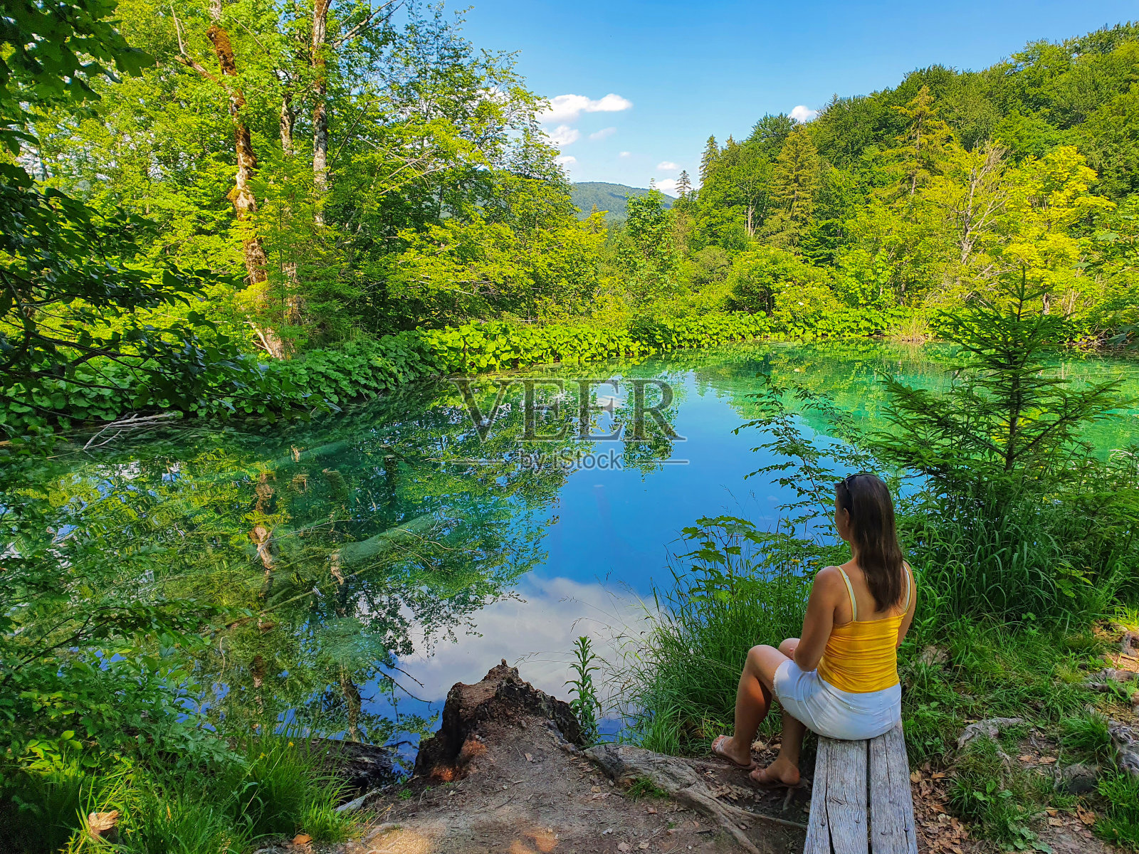 一个陌生的女人坐在一张木凳上，可以看到翡翠湖的景色。照片摄影图片