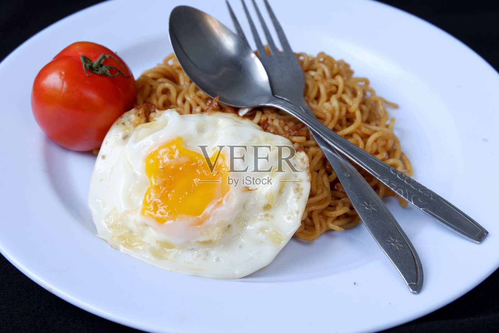 油炸方便面，鸡蛋和西红柿在盘子里，在黑色的背景照片摄影图片