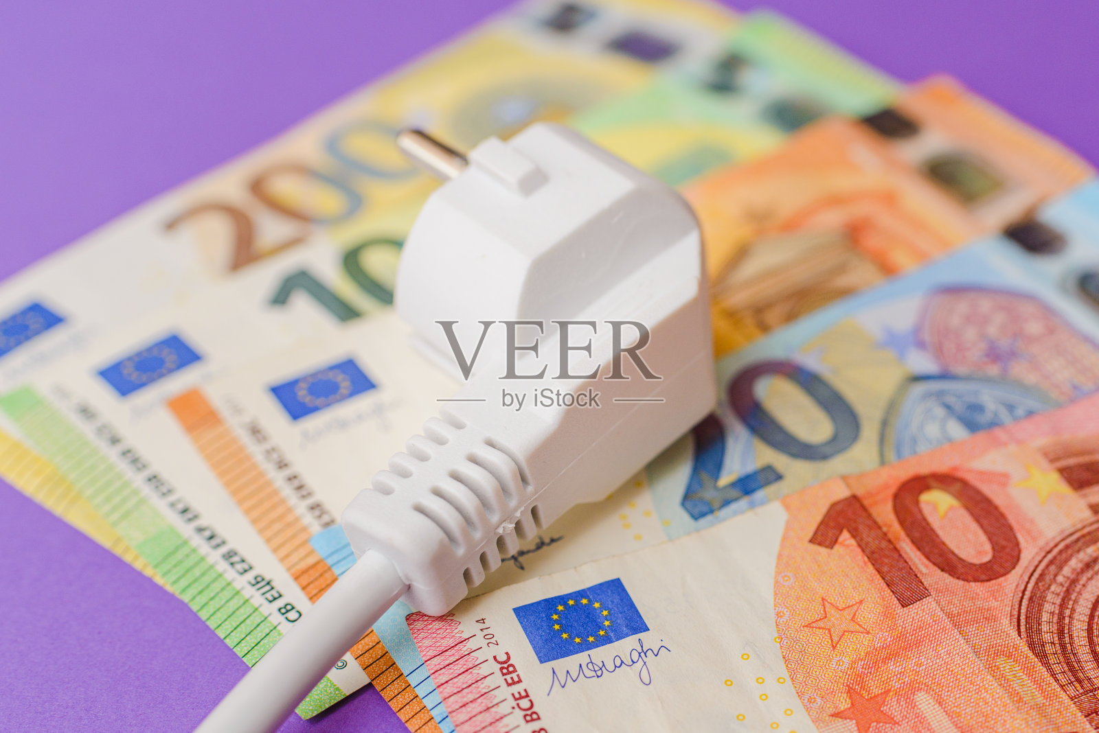 电插头，欧元纸币钞票。紫色在室内背景。电力成本增加对所有居民和企业用户，昂贵的能源账单和电价上涨的概念。照片摄影图片