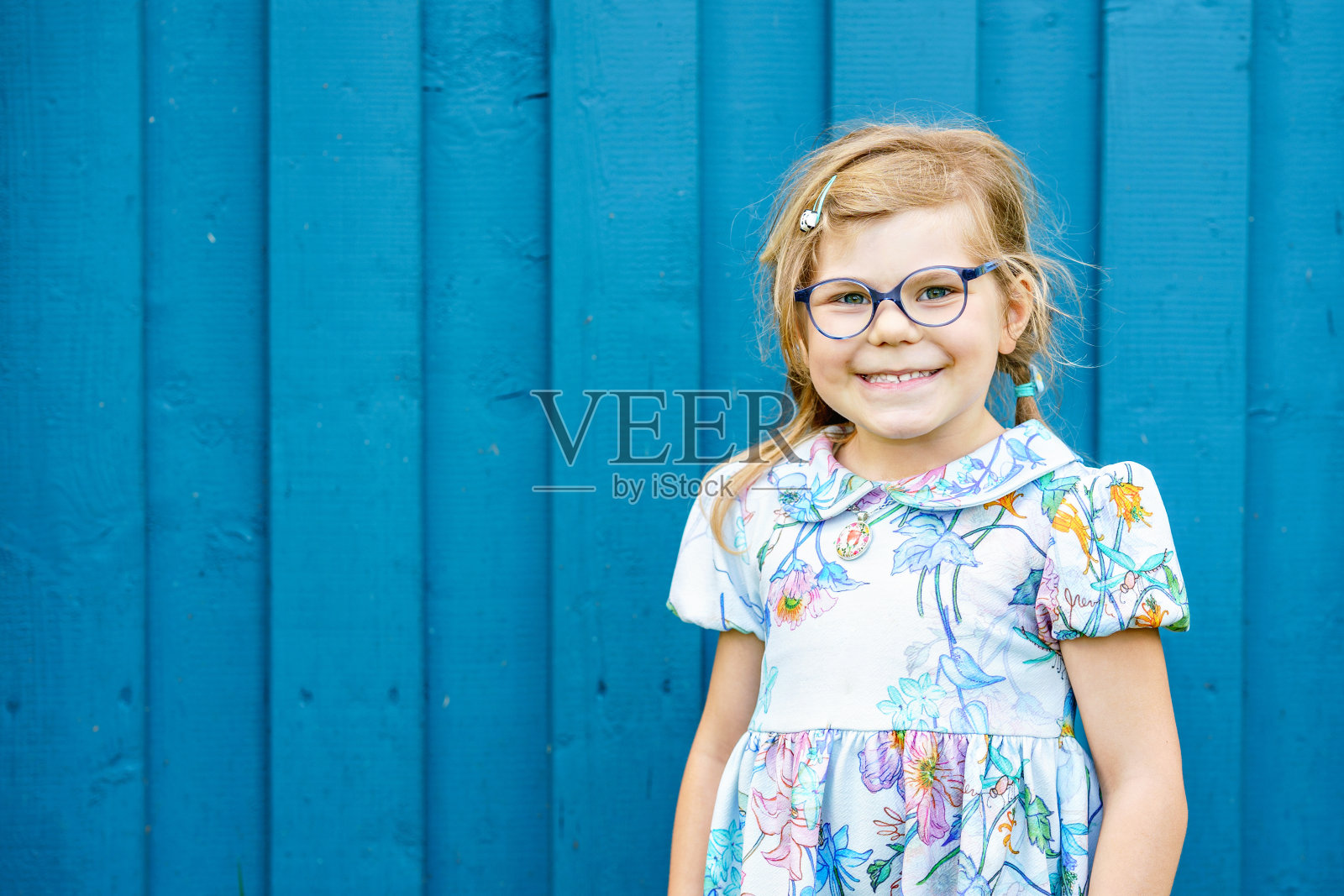 幸福微笑的肖像蹒跚学步的女孩在户外蓝色衣服。一个金发的小孩看着镜头微笑着。快乐健康的孩子喜欢户外活动和玩耍。照片摄影图片