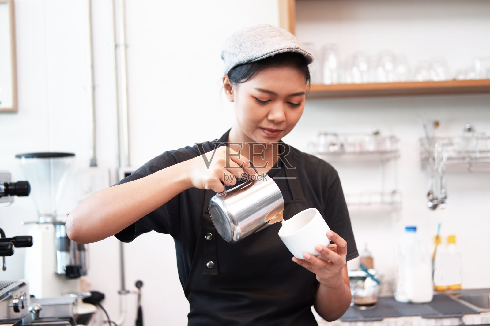 在咖啡吧柜台，微笑的亚洲年轻女咖啡师根据顾客的要求将热黑咖啡倒入白色的杯子中。照片摄影图片