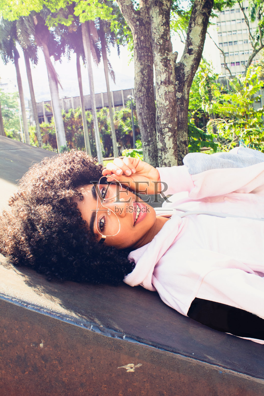 留着爆炸头戴眼镜的漂亮女孩躺在公园里看着镜头照片摄影图片