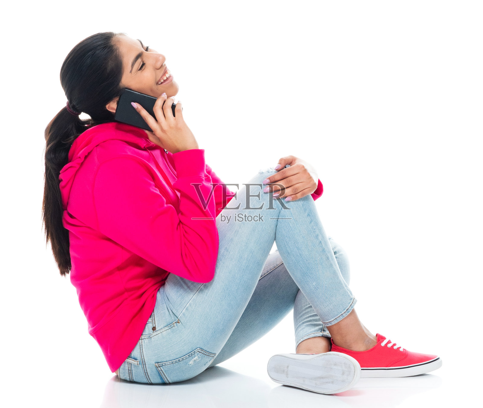 穿着长裤坐在白色背景前，用智能手机的z一代年轻女性照片摄影图片