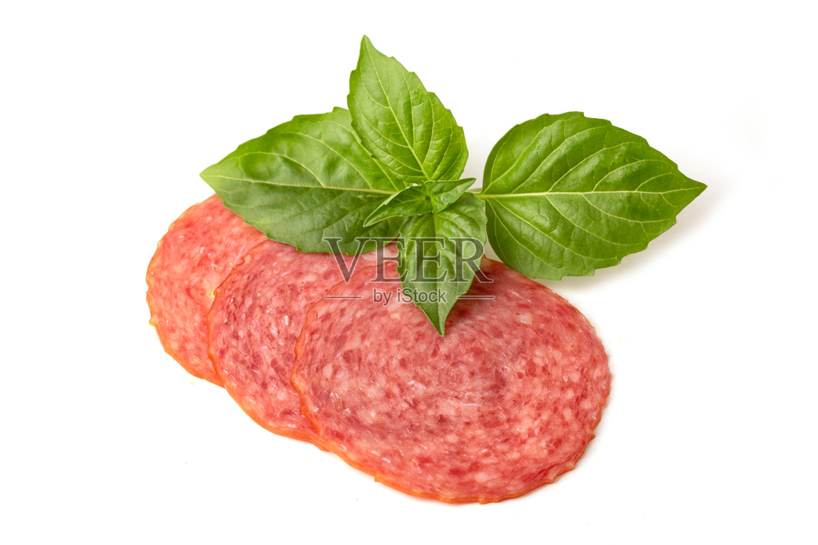 切成圆形的意大利腊肠，白底放罗勒叶照片摄影图片