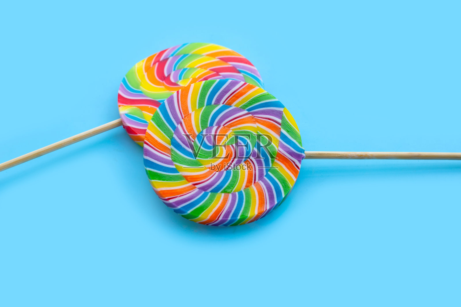 蓝色背景上的彩虹棒棒糖。照片摄影图片