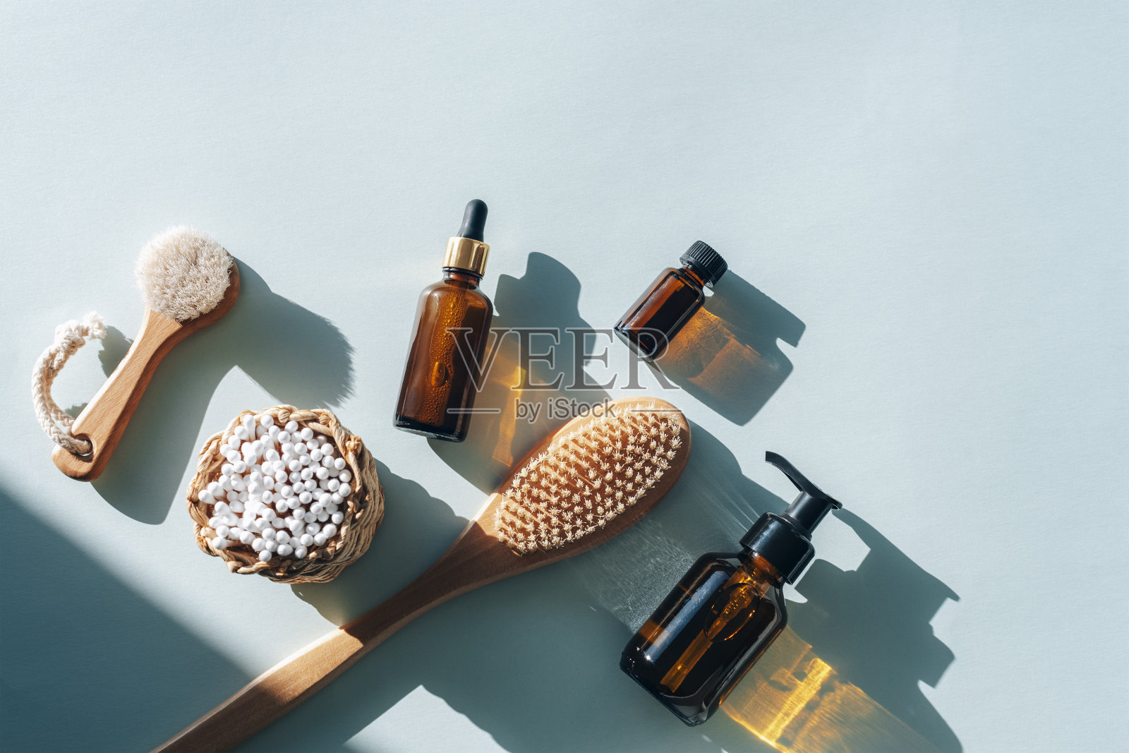 天然化妆品，木制刷子，耳朵清洁棒，棕色玻璃化妆瓶浅蓝色的桌子上硬阴影。“零浪费”的概念。俯视图，平铺照片摄影图片