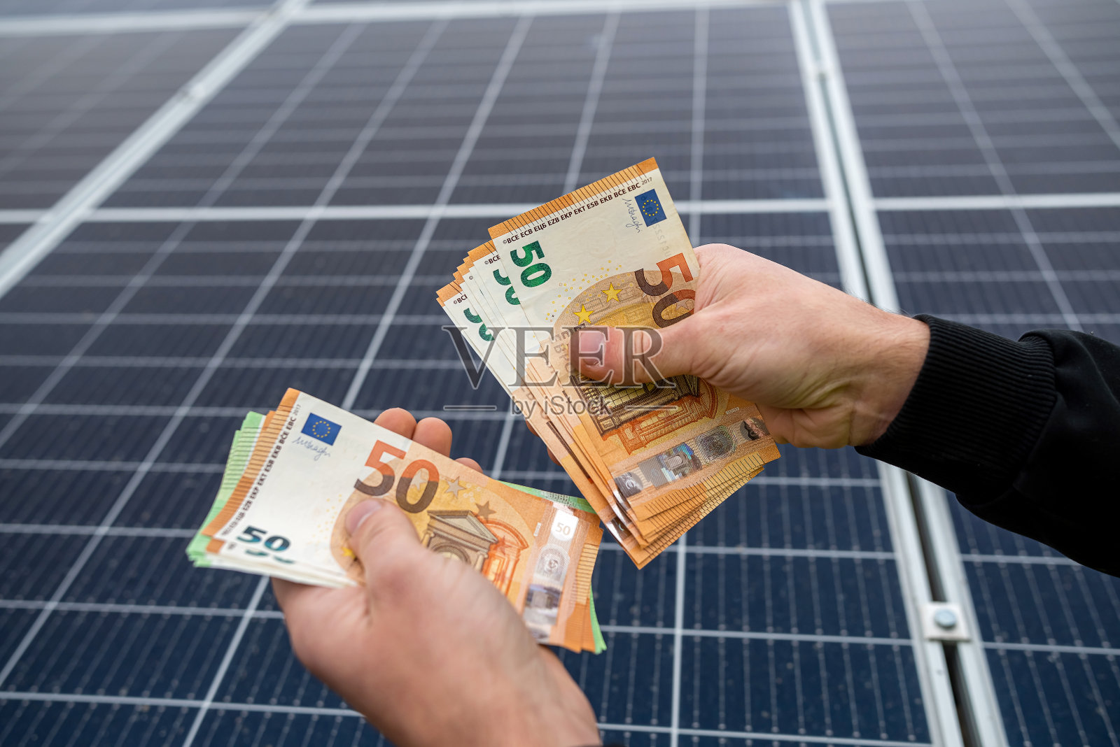 在安装好的太阳能电池板旁，年轻漂亮的双手捧着一大笔欧元。照片摄影图片
