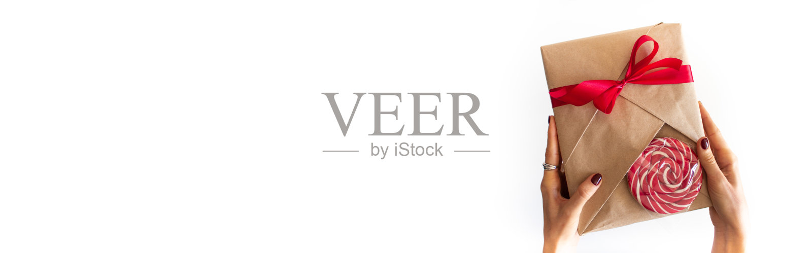 女性手里拿着一个礼品盒，在白色的背景上拷贝空间。一个美甲漂亮的女孩拿着一个用牛皮纸包裹的礼品盒，上面有一条红色缎带。节日横幅与地方的文字照片摄影图片