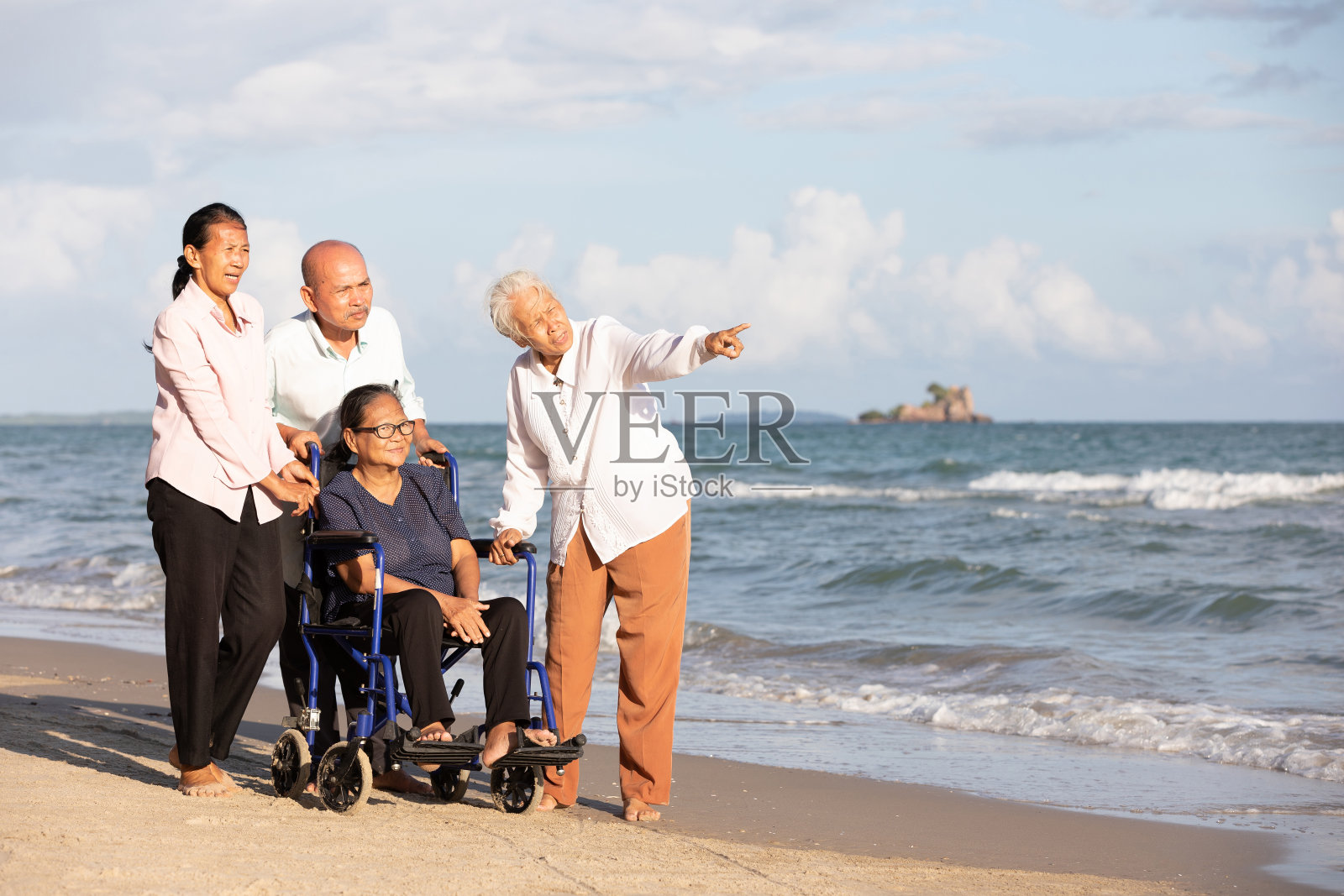 坐在轮椅上的老年妇女和朋友一起在海滩上散步照片摄影图片
