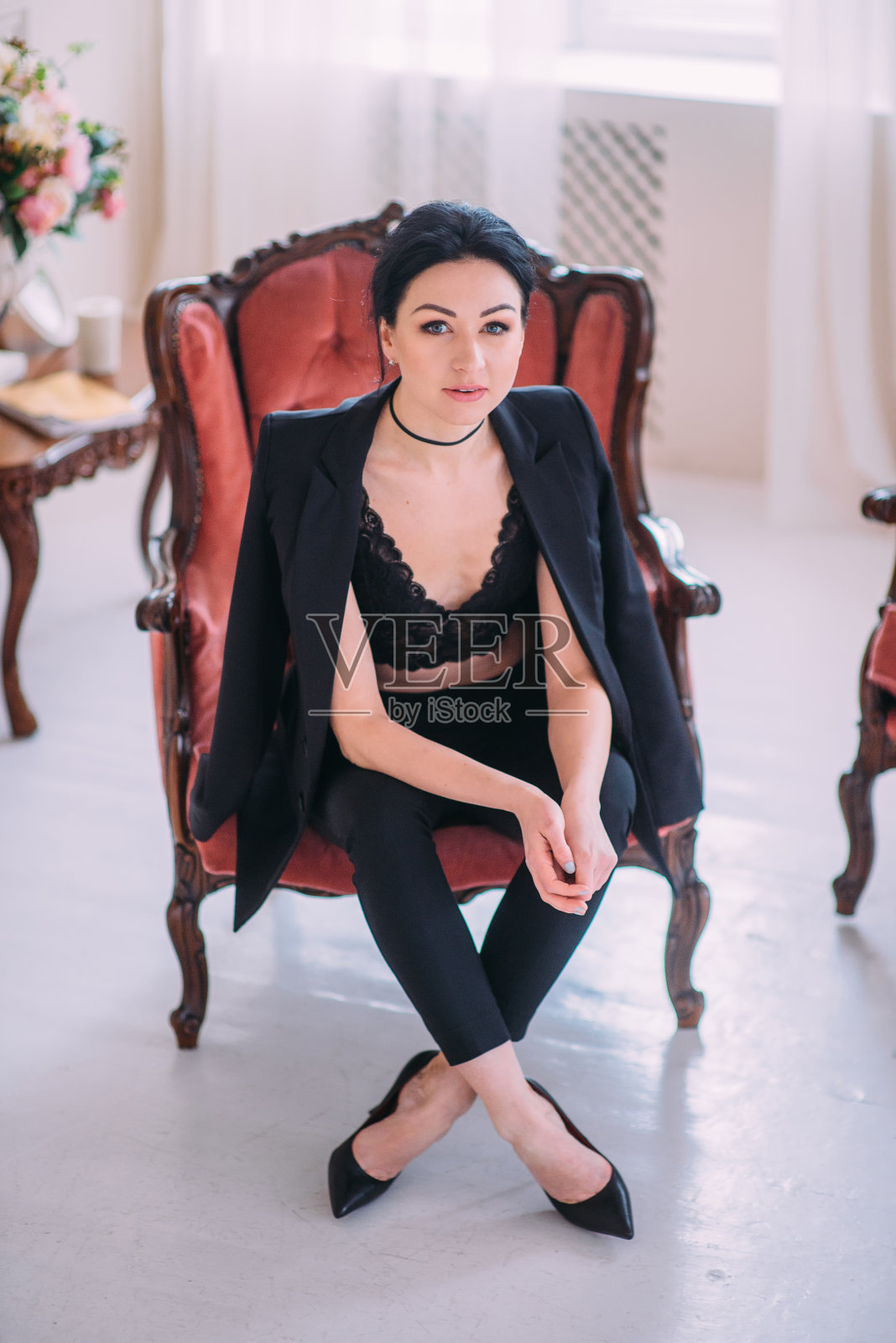 一个美丽的性感女人的肖像穿着黑色西装和高跟鞋在扶手椅的经典内部摆姿势。照片摄影图片