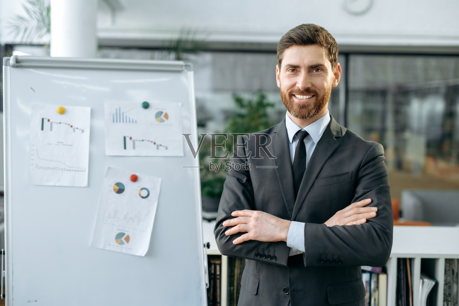 聪明有影响力的白人商人、高管、市场营销人员、年长经理，穿着正装，站在带着图表的白板旁，在一个现代化的办公室里，看着镜头，友好地微笑照片摄影图片