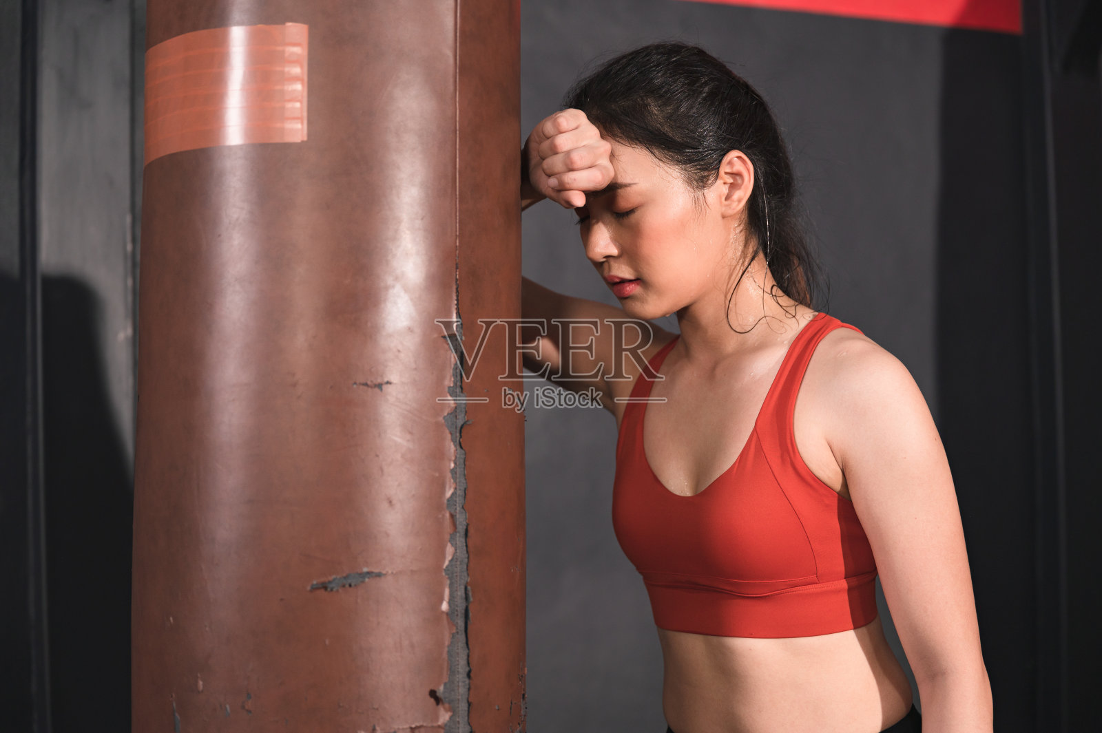 亚洲妇女用拳击沙袋挥汗如雨，疲惫不堪照片摄影图片