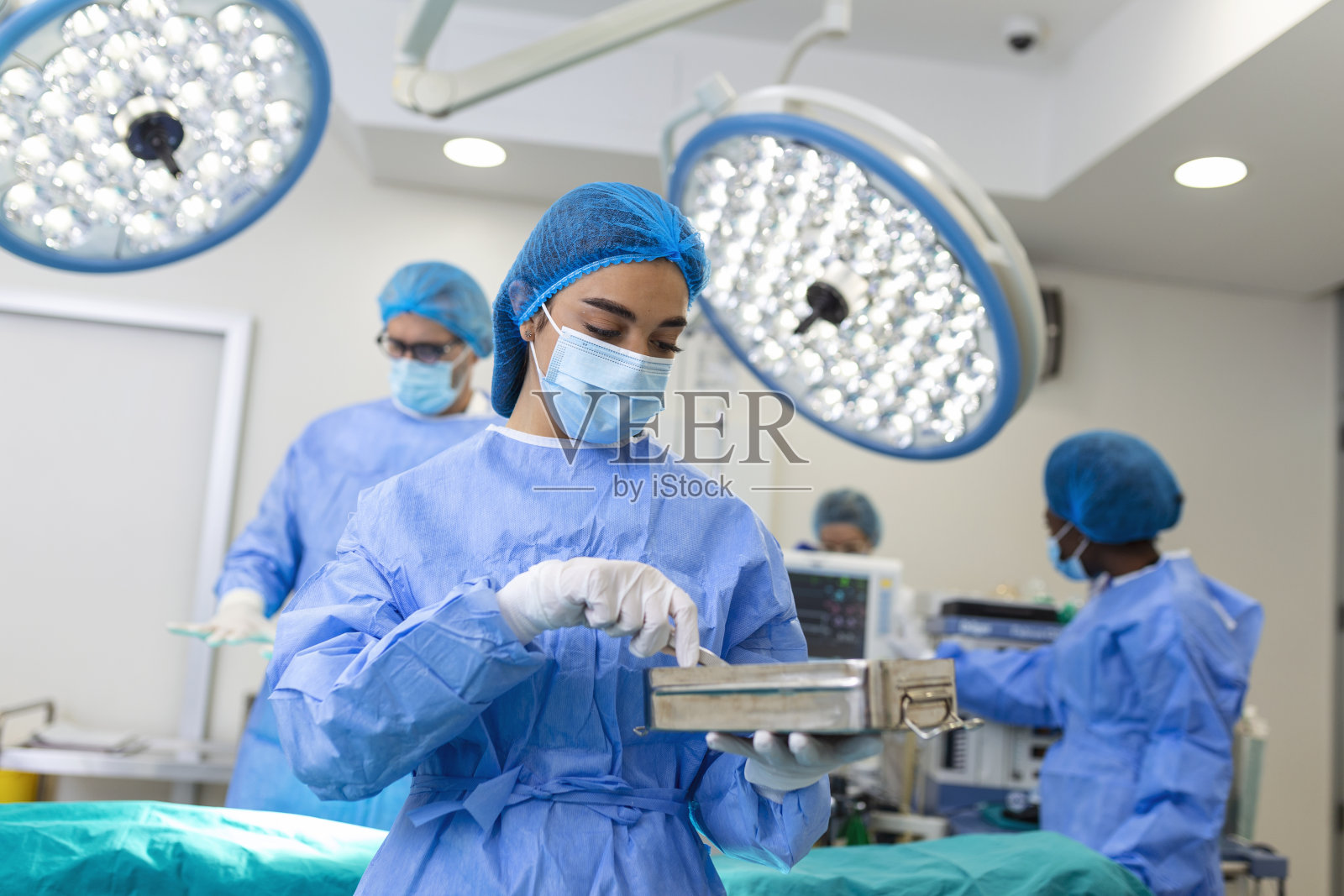 身穿手术服的女外科医生在手术室拿手术器械。医院手术室的年轻女医生照片摄影图片