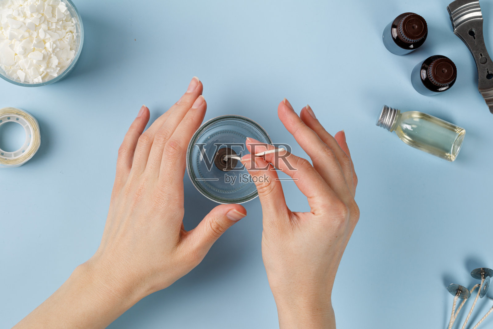 将蜡烛芯装入罐中，制作蜡烛。女人手工制作蜡烛。Flatlay顶视图。蓝色背景照片摄影图片