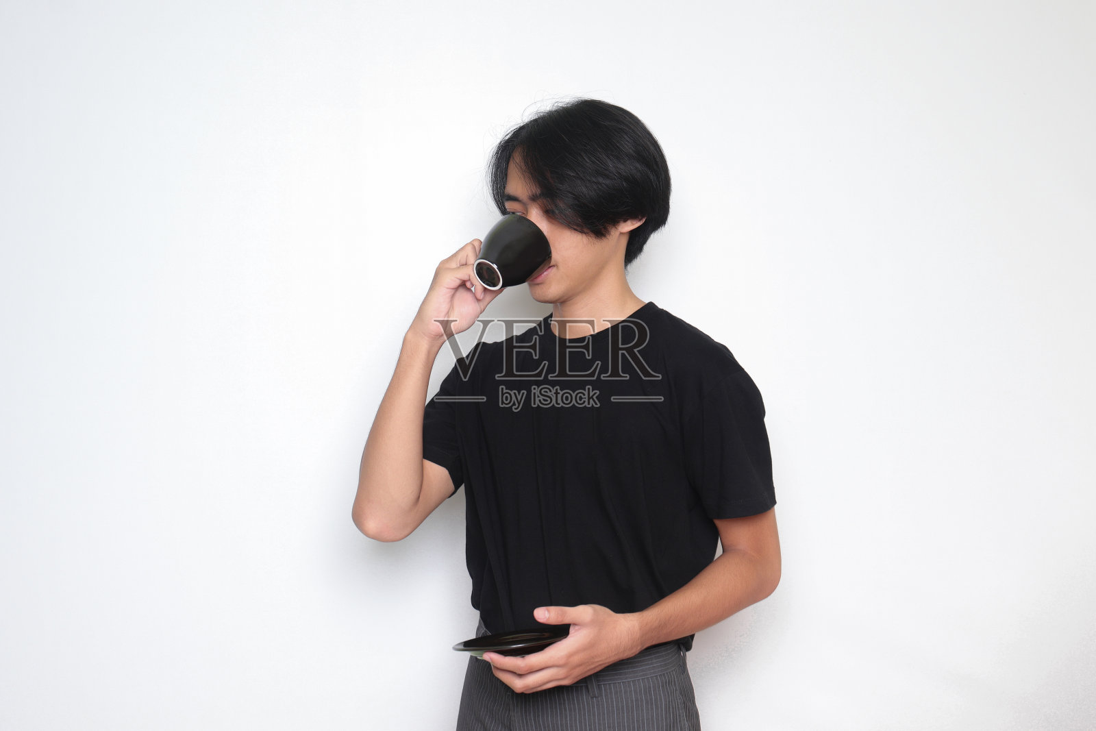 长头发的英俊亚洲男子一边拿着茶托一边喝咖啡照片摄影图片