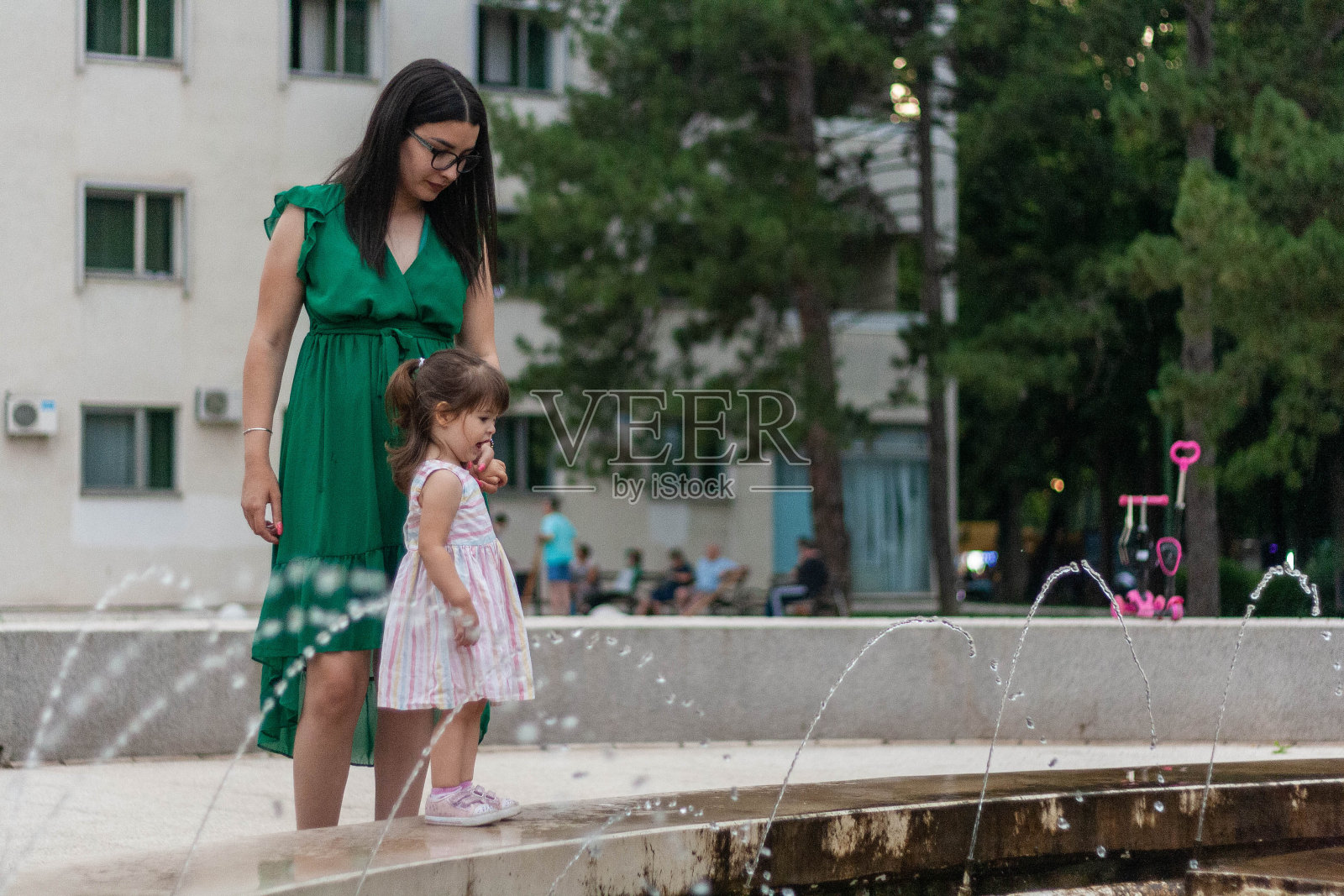 那位妇女(保姆)抱着孩子。孩子想进入喷泉。照片摄影图片