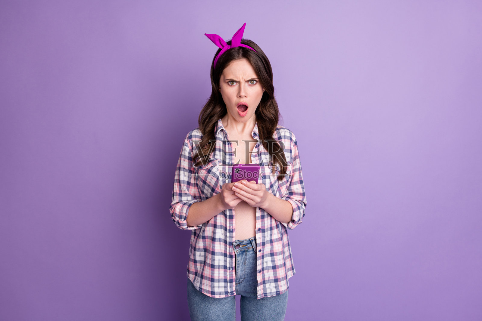 愤怒的愤怒的女孩浏览互联网的照片肖像，带着手机，在生动的紫色背景隔离照片摄影图片