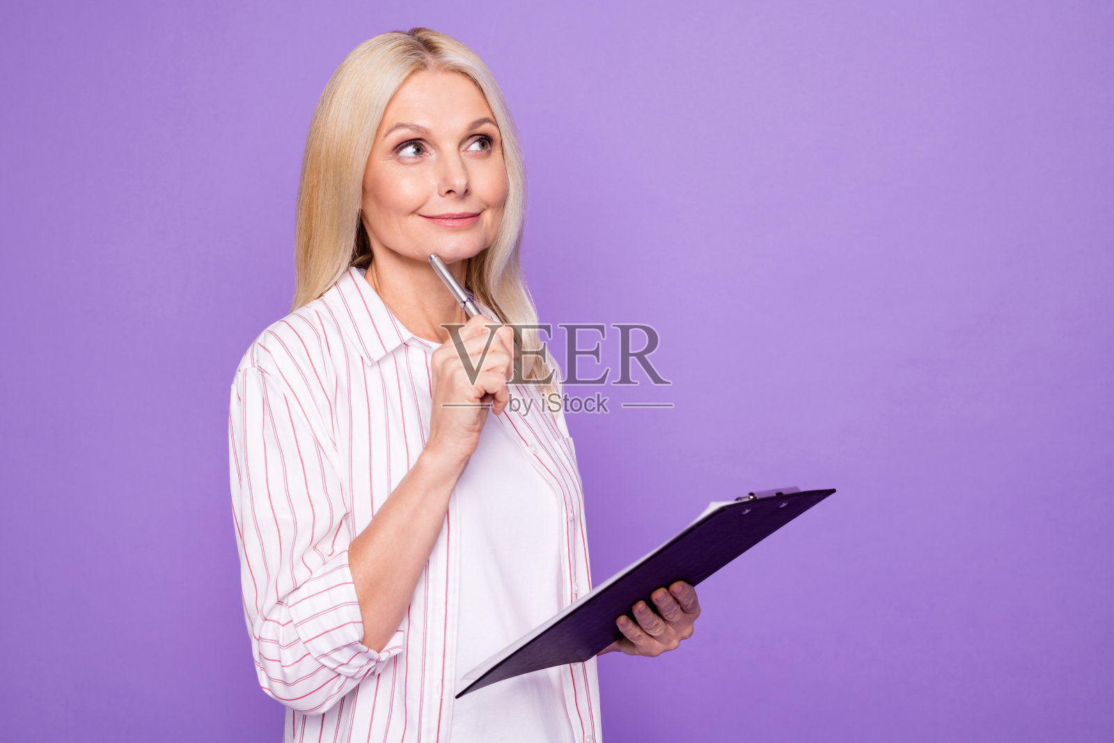 甜蜜的梦想夫人养老金穿条纹衬衫拿着剪贴板的照片，看空空间孤立的紫罗兰色背景照片摄影图片
