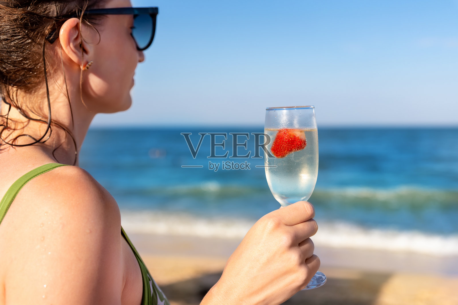 侧视图肖像年轻的成年女子拿着冷酒精刷新饮料玻璃看海滨在夏天的海滨度假。女性在异国情调的度假酒店海滩放松度假照片摄影图片
