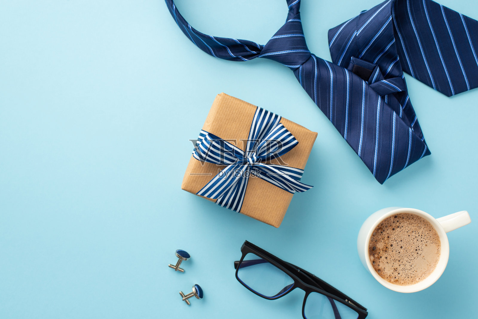 父亲节的概念。顶视图照片的牛皮纸礼品盒丝带蝴蝶结杯咖啡杯袖扣和蓝色领带上孤立的粉彩蓝色背景照片摄影图片