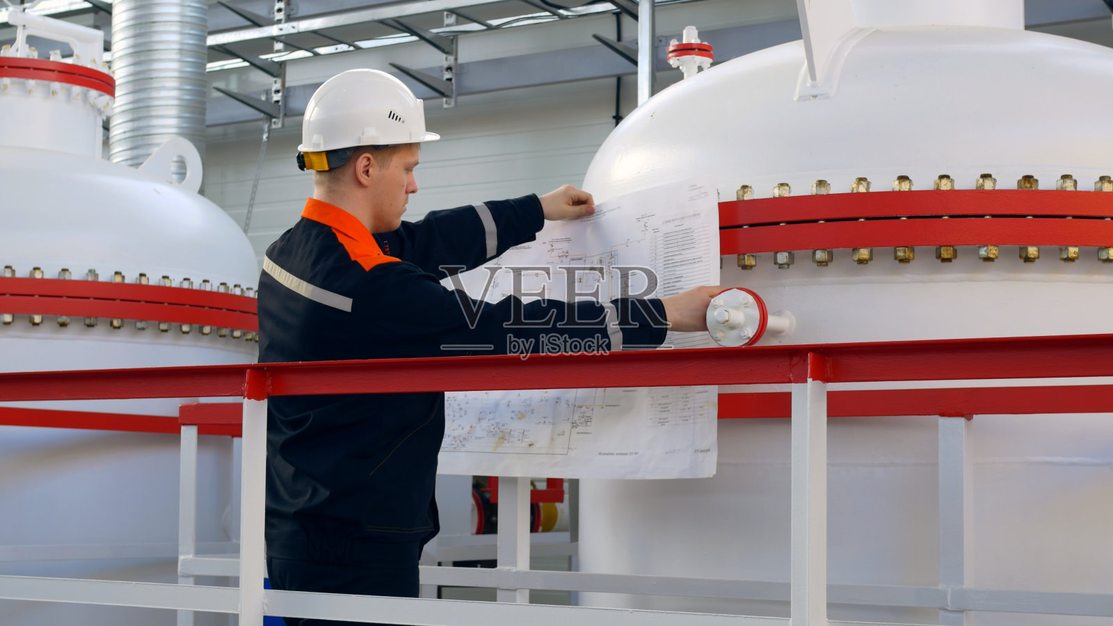 一名戴着白色头盔的工程师手里拿着图纸，参照工艺方案，检查工艺设备和气、液管道。工厂工程师的工作照片摄影图片